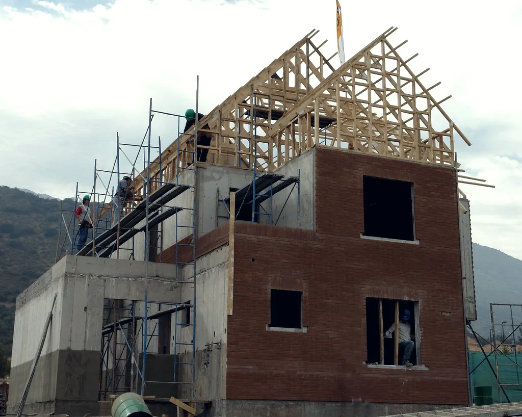 A house under construction, blockwork walls with a timber roof frame going up